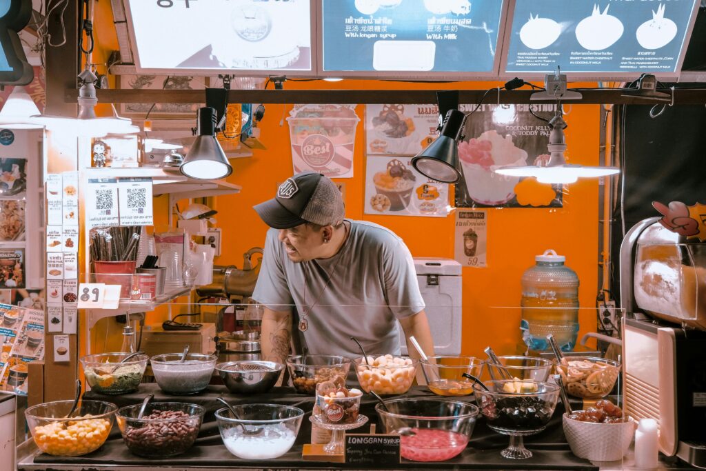 A man serving toppings at a vibrant street food booth indoors. Perfect for lifestyle and culinary themes.